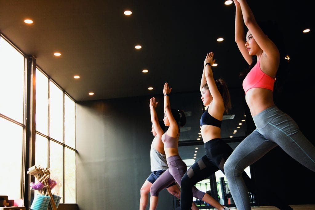 A group of young Asian people who are in good shape studying yoga with a trainer They are in a warrior 1 pose.