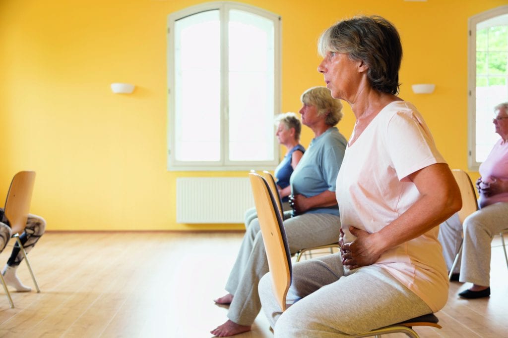 Closeup of active senior women yoga class on chairs, doing breathing exercise, hands on abdomen to feel the movement of breath